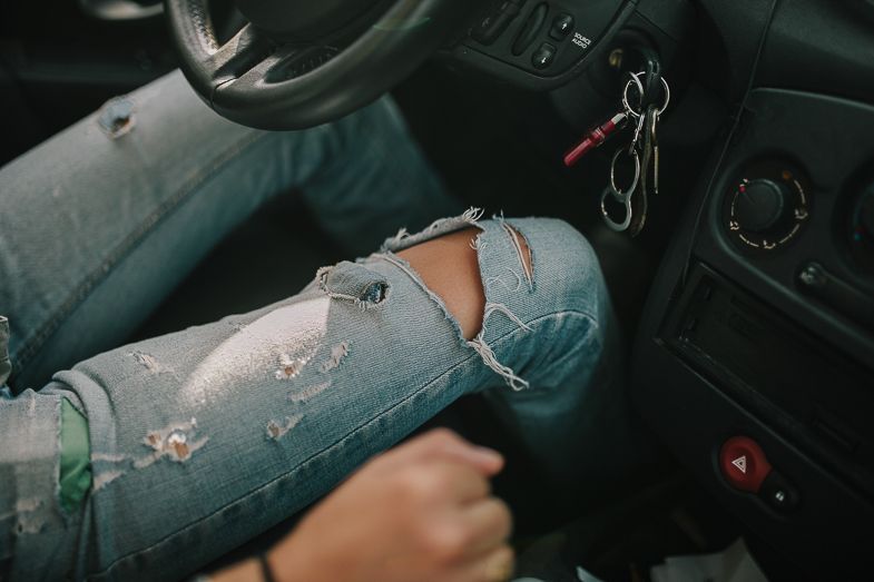 Close-up of distressed denim jeans inside a car interior with keys visible.