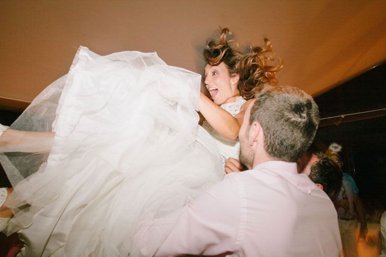 A celebratory moment as a bride in a white gown is lifted high during a wedding reception.