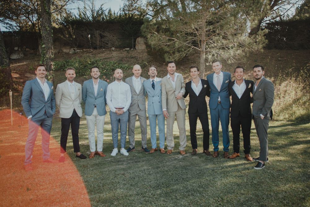 Wedding party group photo of groomsmen wearing coordinated suits in shades of blue and gray outdoors.