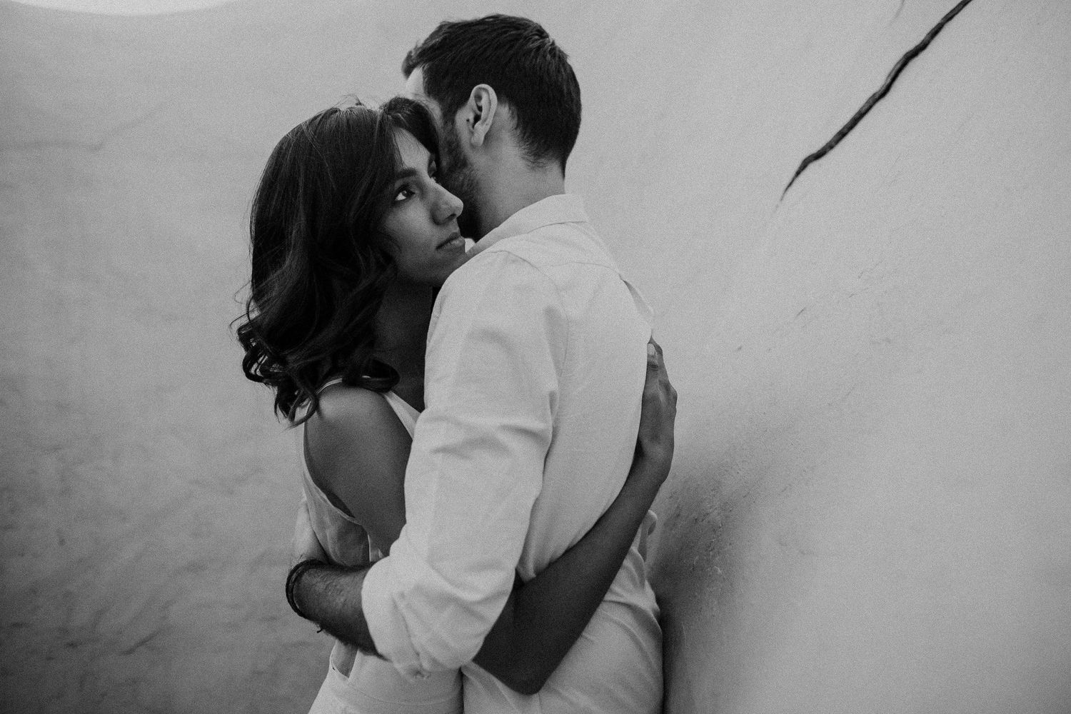 Intimate black and white portrait of a romantic couple against a white wall.