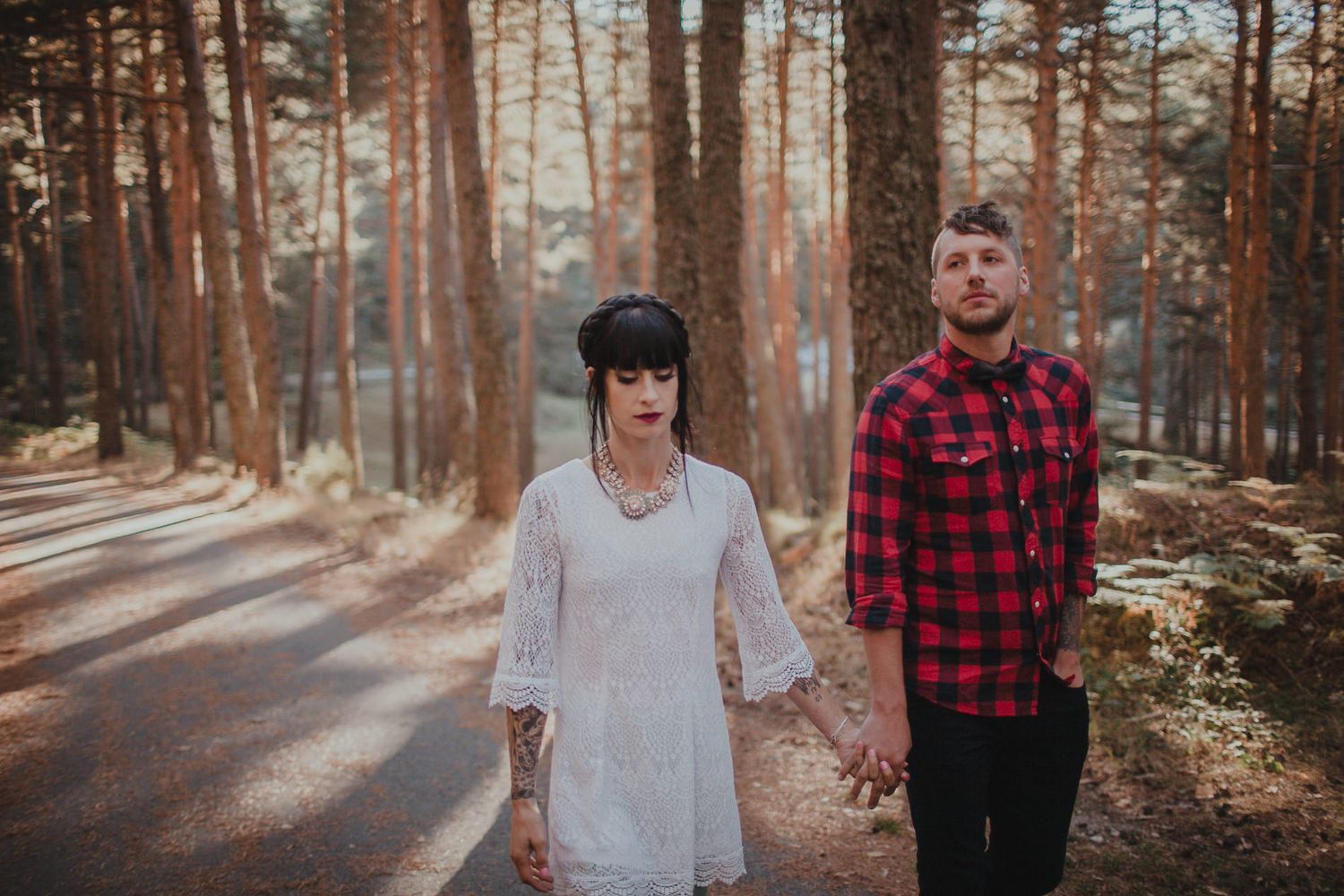 Couple in contrasting outfits standing together on forest path among tall pine trees.