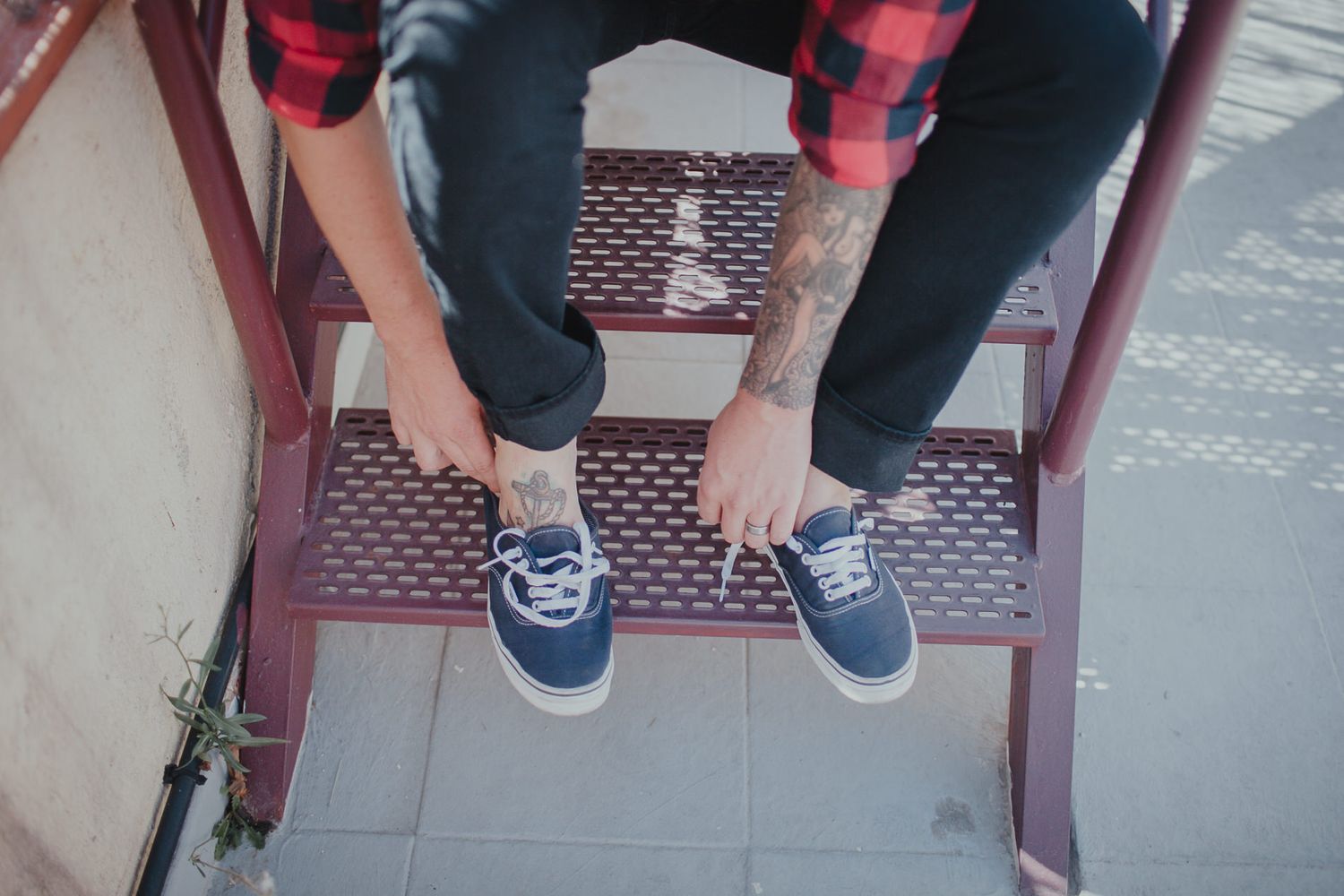 Person wearing red plaid and blue sneakers sitting on metal steps.