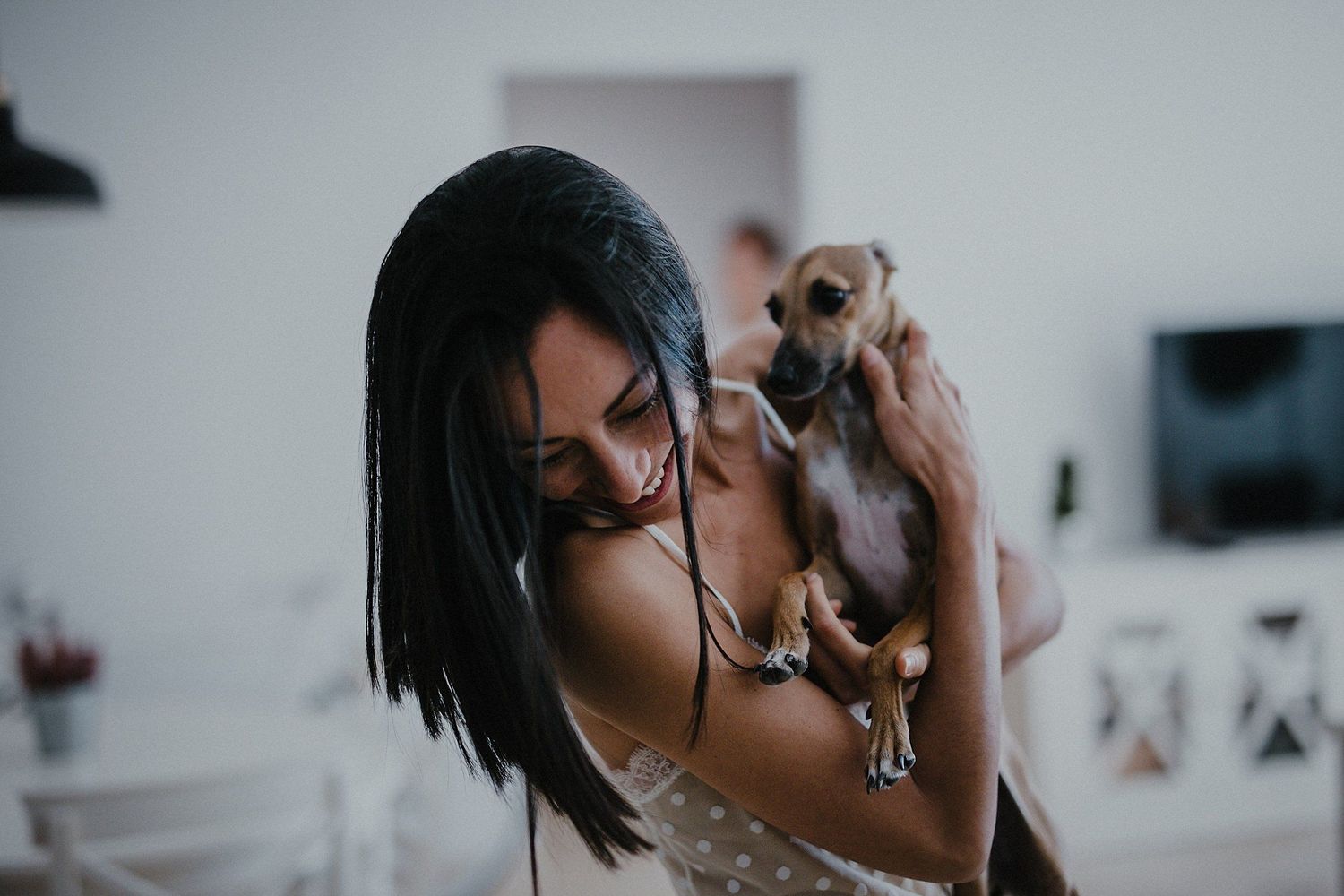 Woman in lace dress holding small dog in modern home setting.