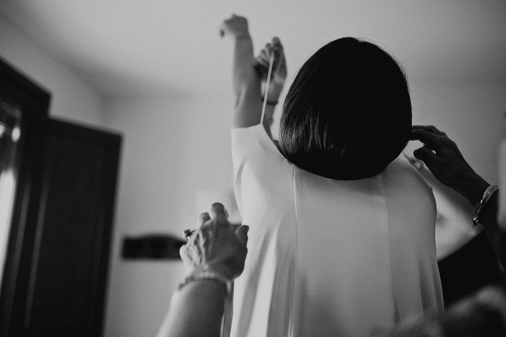 Black and white image showing silhouette of someone with raised arms getting dressed.