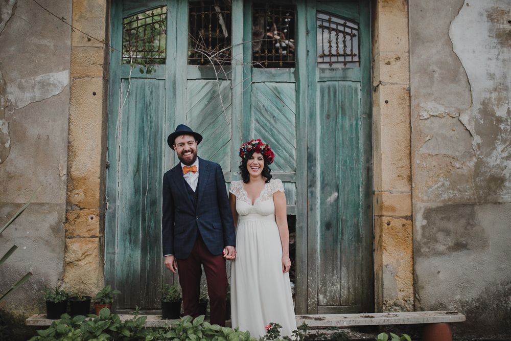 A couple stands in front of weathered turquoise doors wearing vintage-inspired wedding attire.