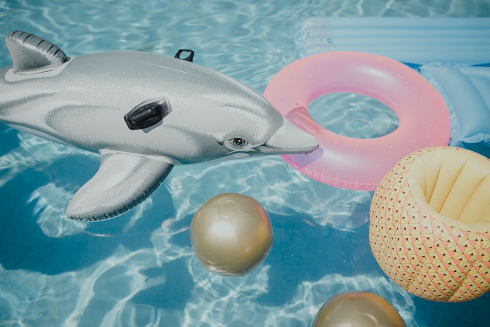 Inflatable pool floats including dolphin and pink ring floating in blue swimming pool water.