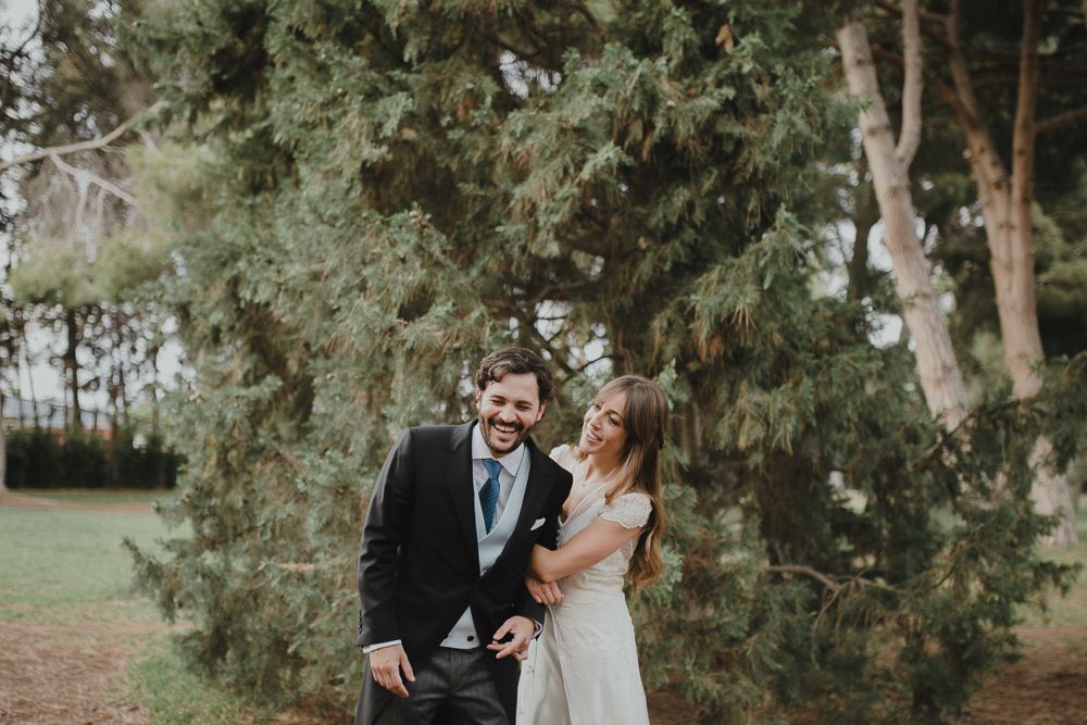 Wedding couple sharing laughter among evergreen trees in outdoor setting.