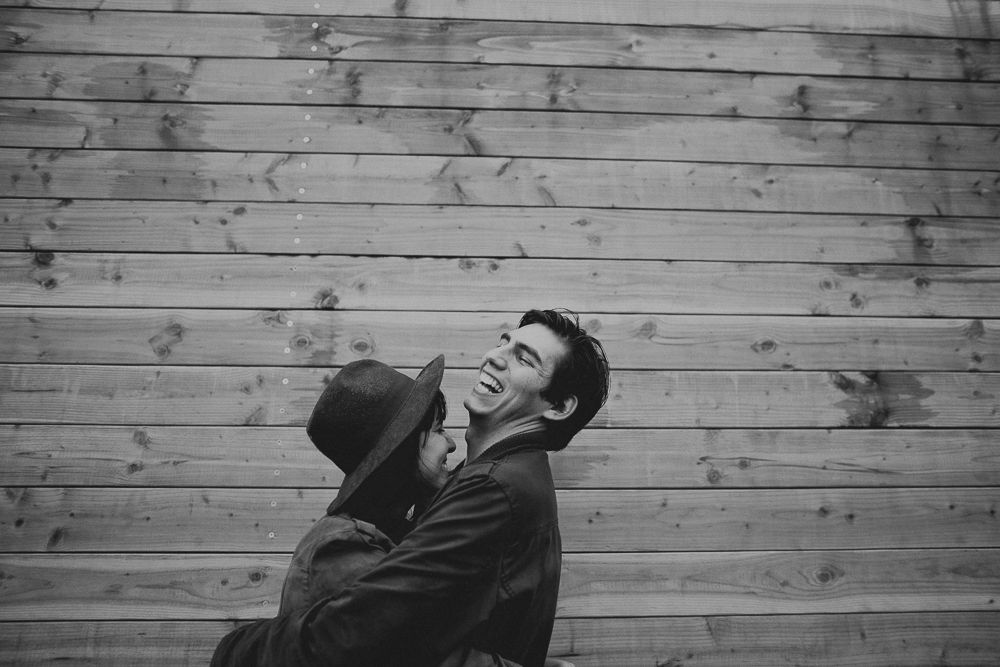A candid black and white moment of shared laughter against weathered wood siding.
