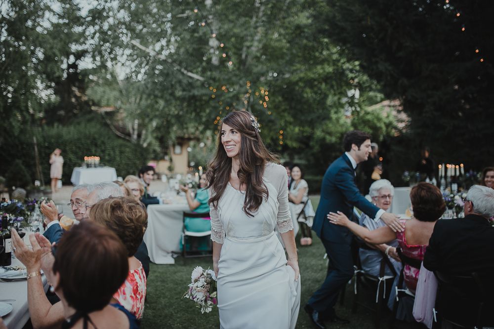 Wedding attendees celebrate and dance at an outdoor reception under tall trees.