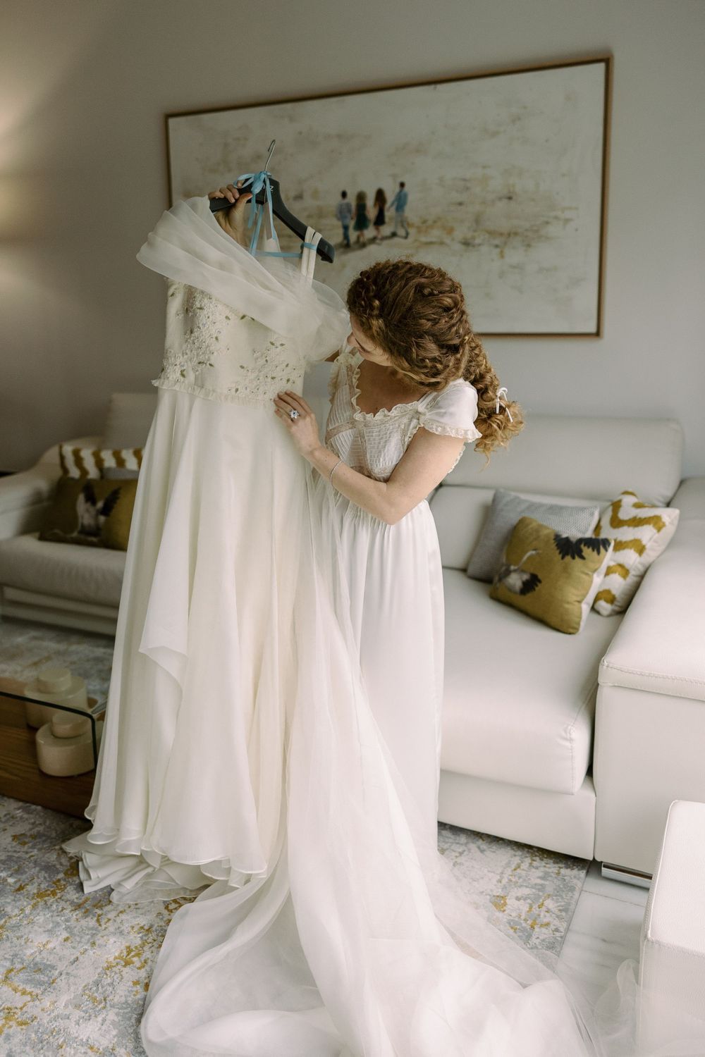 A wedding dress being prepared in a bright, modern room with decorative pillows.