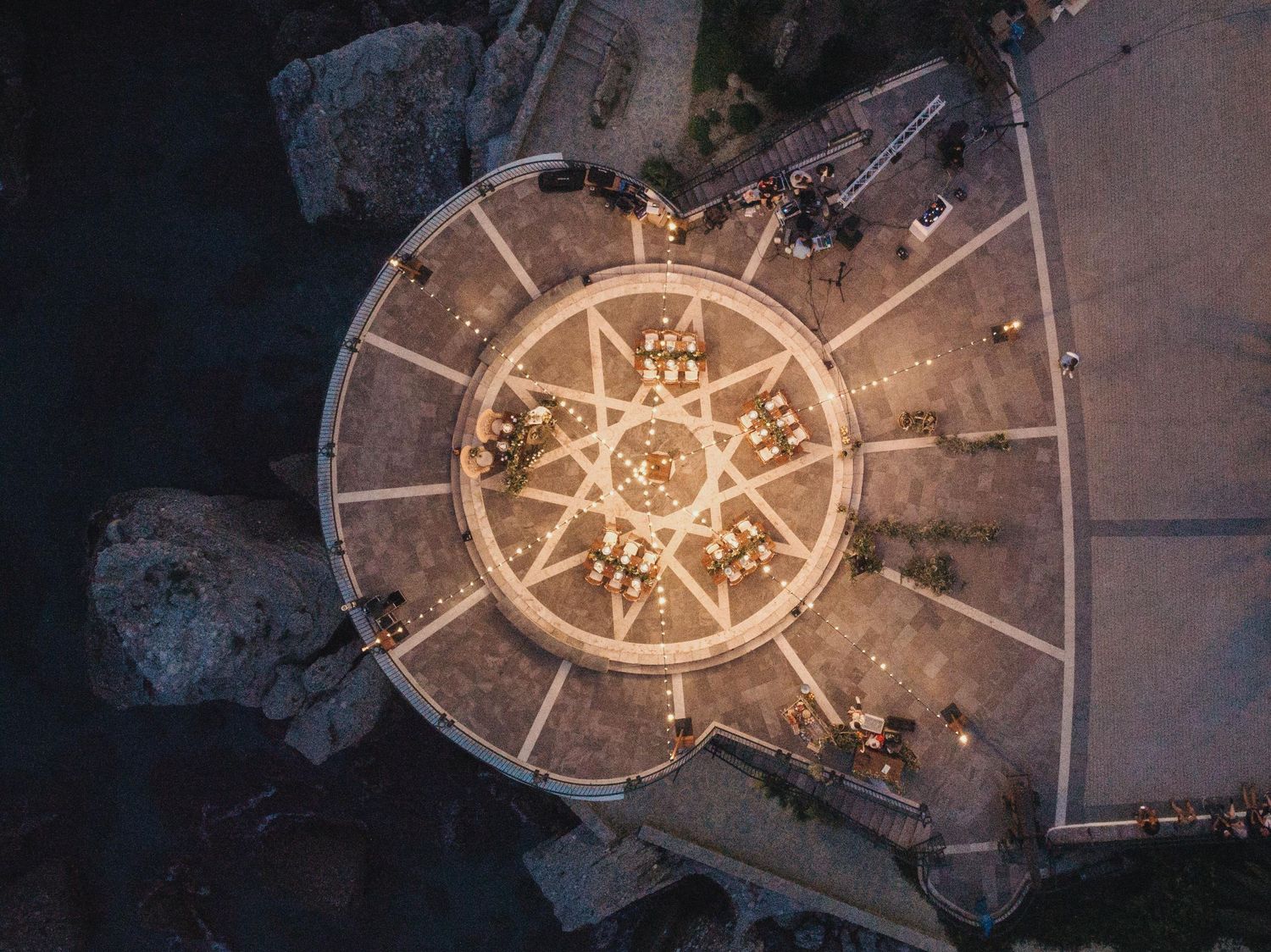 Aerial view of a circular plaza with glowing lights arranged in a compass-like pattern at night.