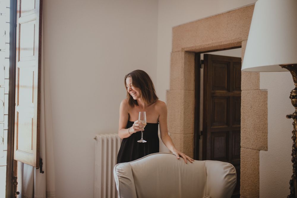 Person in black dress leaning against white armchair near window.