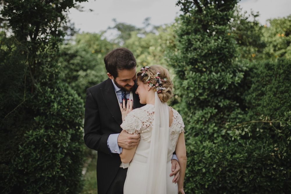 A romantic outdoor wedding portrait with couple embracing against garden greenery.