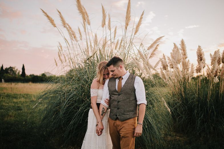 A tender moment between a couple standing by tall ornamental grasses at dusk.