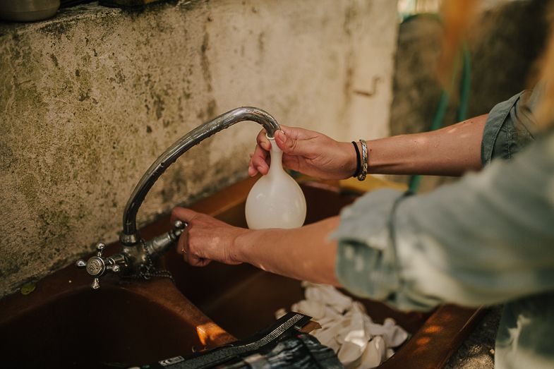 Hands filling a water bottle from a rustic outdoor faucet.