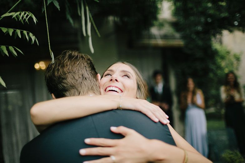 A joyful embrace captured during an outdoor wedding celebration with guests in the background.