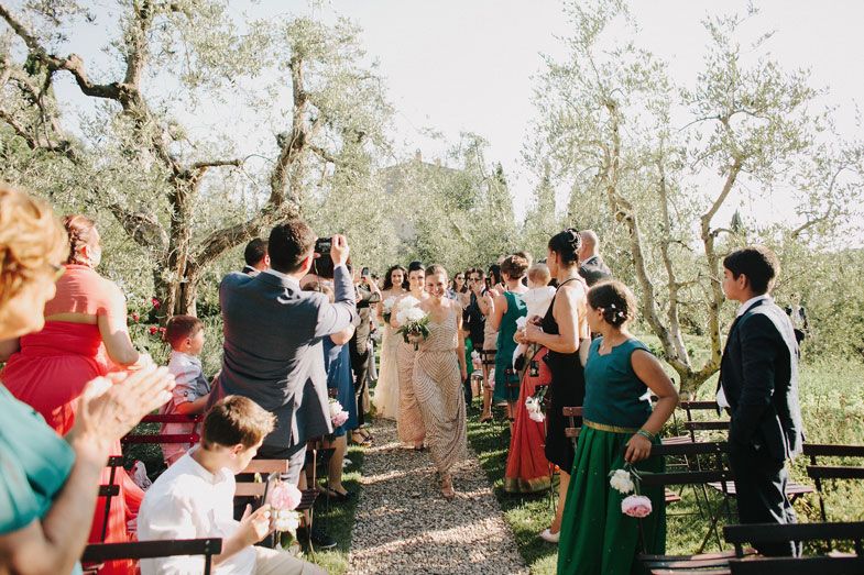 Wedding guests gathered along olive tree-lined path during outdoor ceremony.