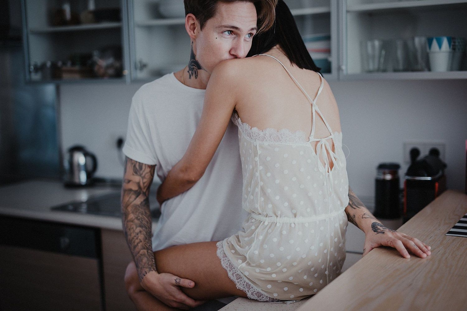 Couple in casual attire embracing intimately in modern kitchen setting.