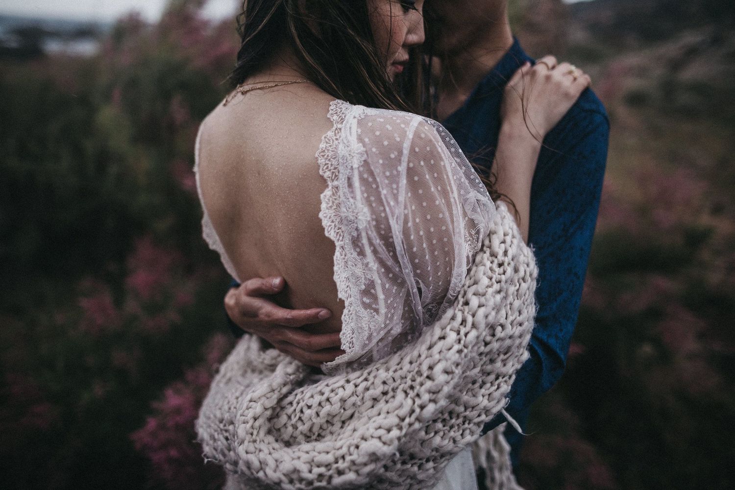 Detail shot of delicate white lace dress back with couple embracing.