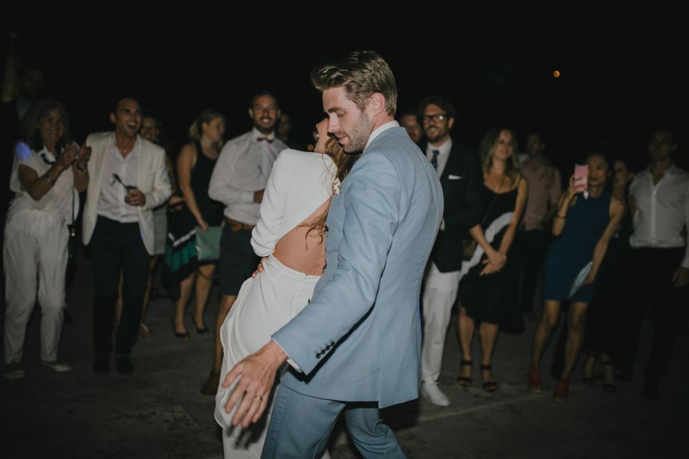 A couple dances at an outdoor evening celebration while guests watch in background.