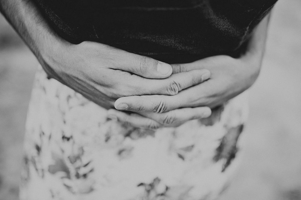 Close up black and white shot of hands resting on a patterned dress fabric.