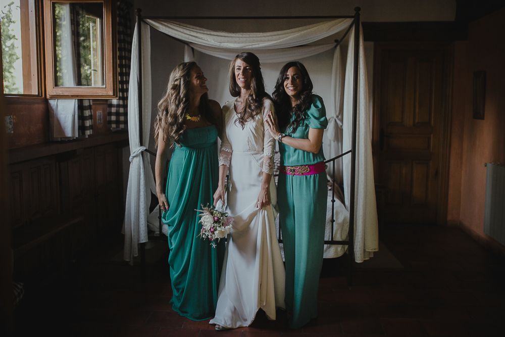 Wedding party poses in front of white fabric backdrop, with bridesmaids in teal green gowns.