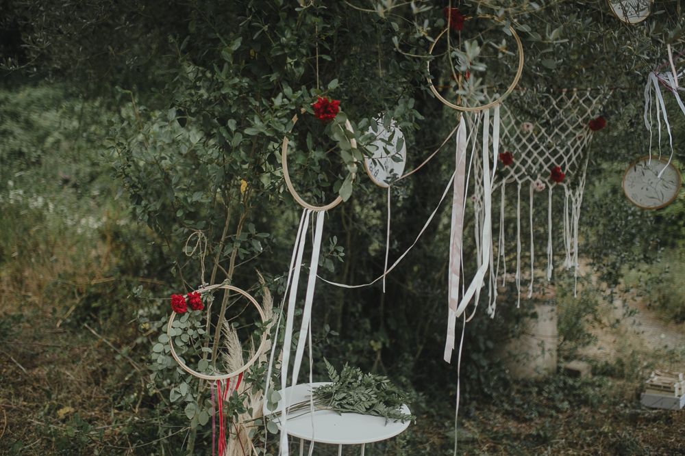 Bohemian dreamcatchers with red flowers hang in garden setting.