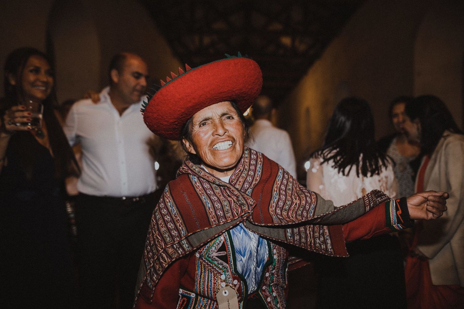 Person in traditional red beret and poncho dances enthusiastically at indoor celebration.
