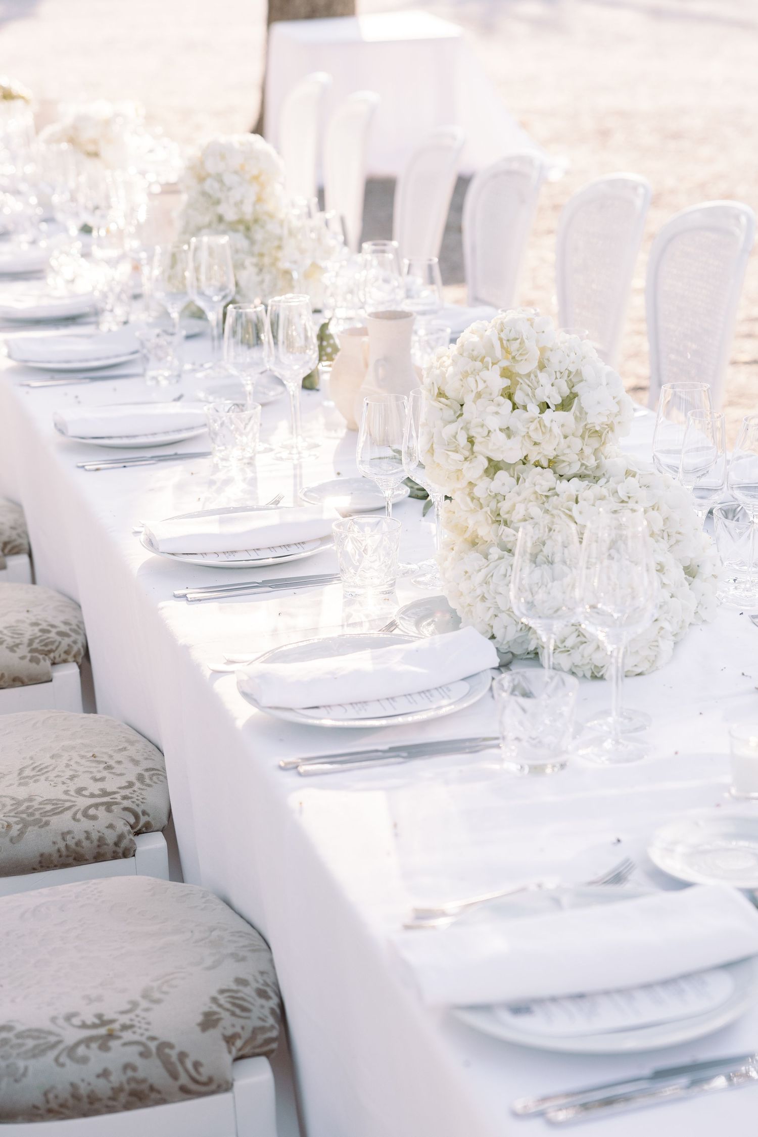 Elegant white wedding table setting with hydrangea centerpieces and crystal glassware.