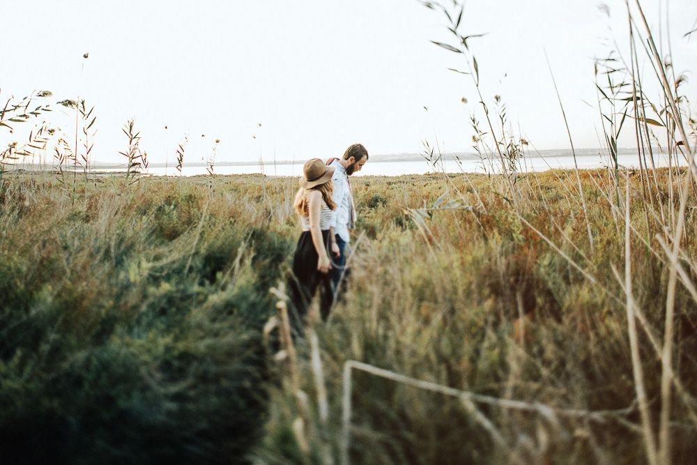 A couple walks through tall grass in a scenic field at dusk.