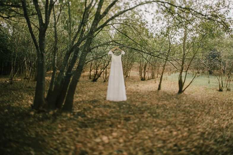 A white wedding dress hangs ethereally between trees in a woodland setting.