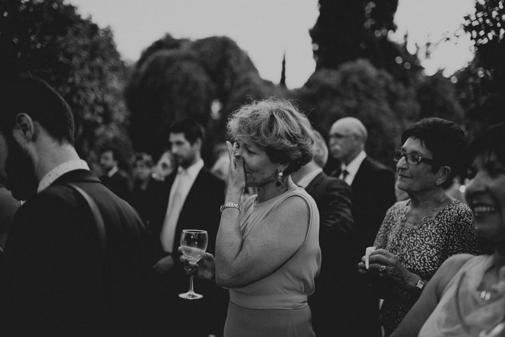 Black and white candid of wedding reception guests enjoying champagne outdoors.
