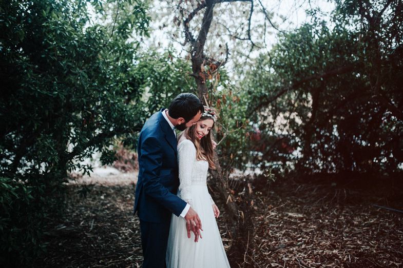 Romantic wedding photo in wooded setting with natural light filtering through trees.