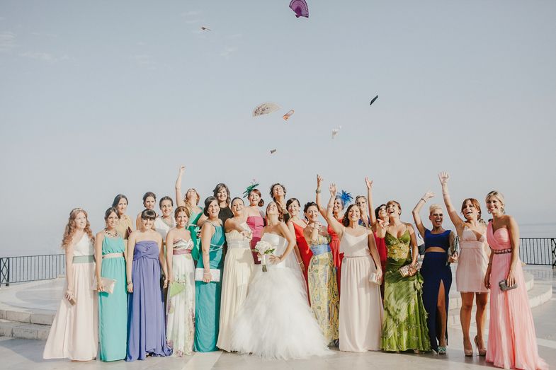 A wedding party in pastel dresses throws colorful flower petals in celebration.
