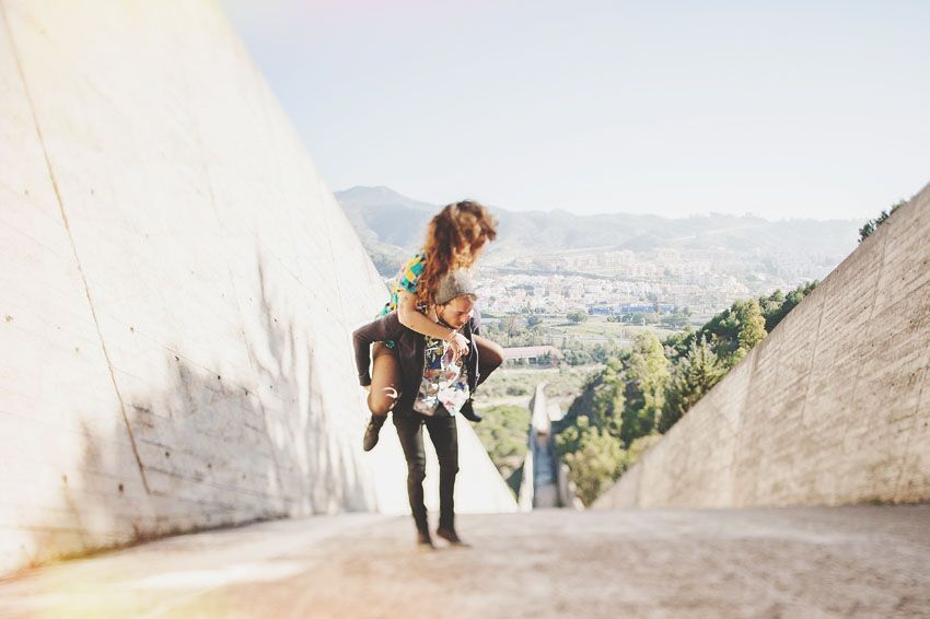 A person holds a small dog while standing on a concrete path overlooking a valley landscape.