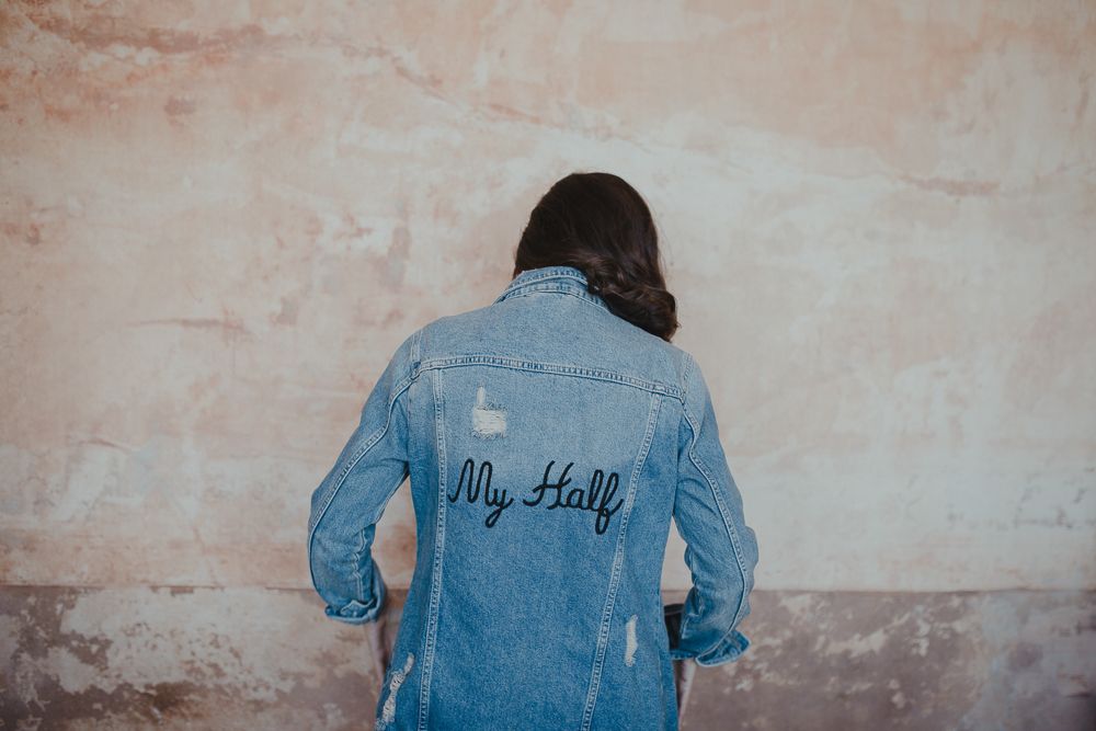 Back view of denim jacket with text embroidery against pink wall.