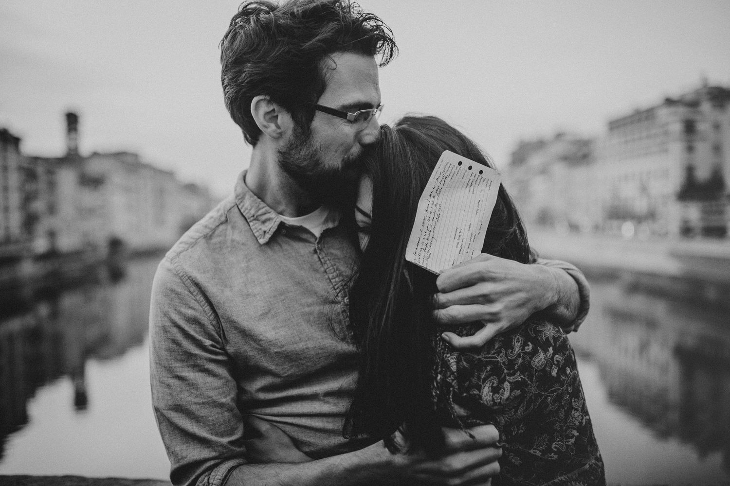 Couple shares an intimate moment while reading a document along the Arno River in Florence.