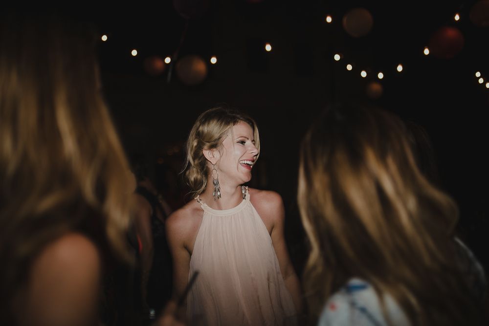 Woman smiles among friends under glowing string lights at evening celebration.