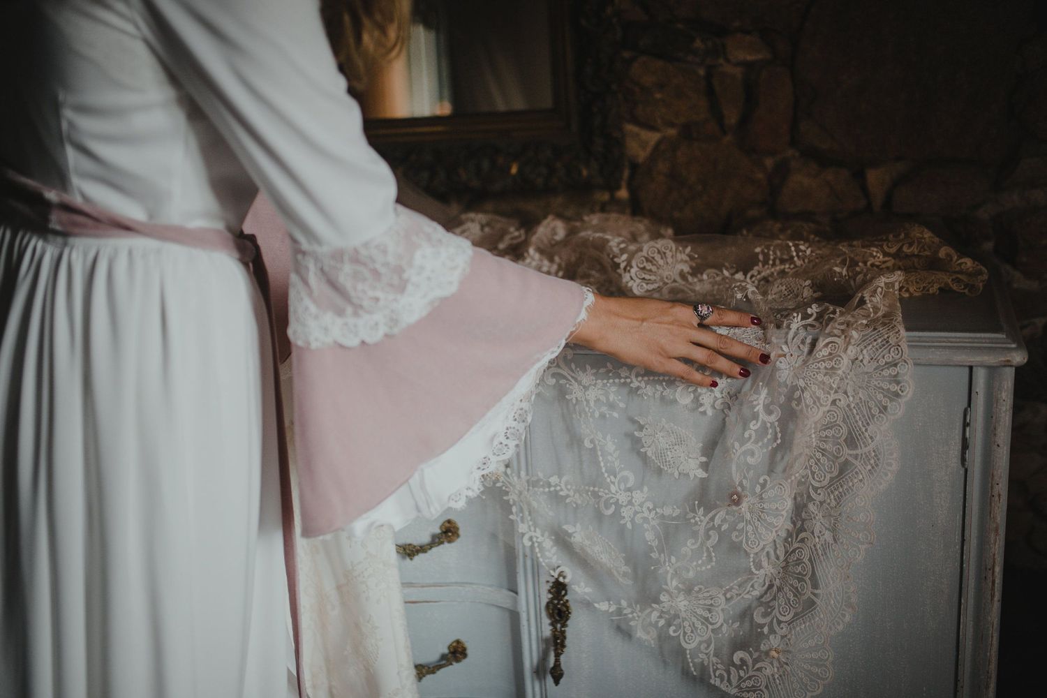 Delicate white lace details of a vintage-style dress being gently touched against a rustic background.