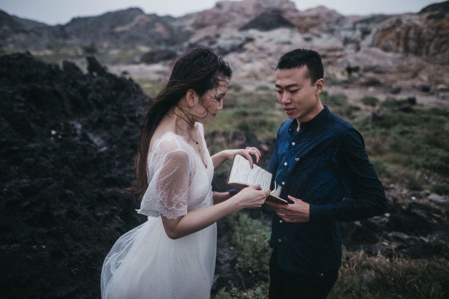 A couple reads from written papers together in an atmospheric outdoor setting.