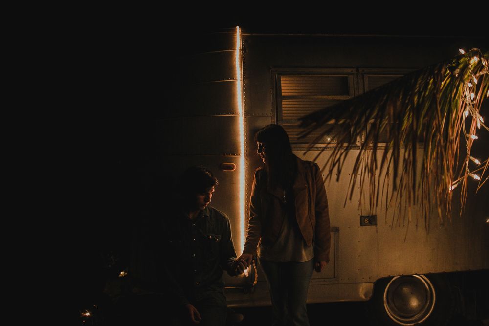 Dramatic nighttime scene with light beams and shadows against a vintage trailer.
