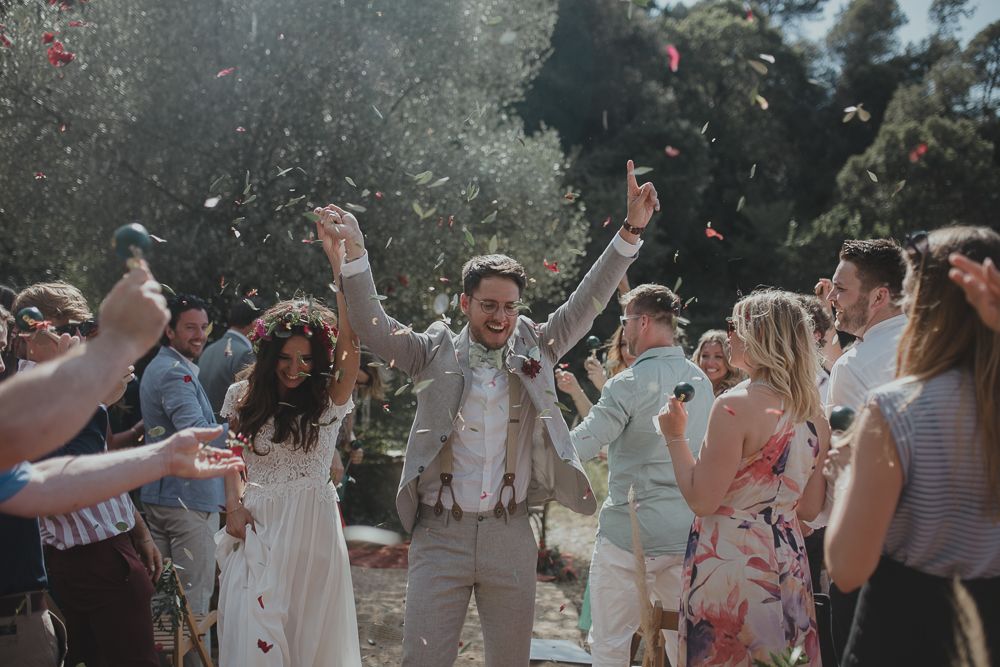 Joyful celebration with flower petals being tossed in the air at an outdoor wedding.