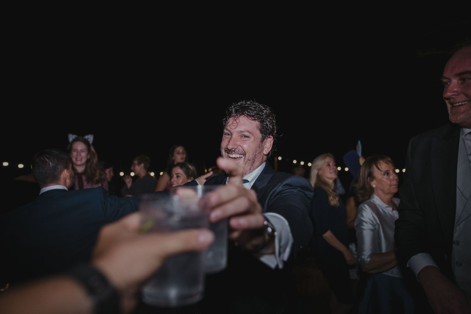 Wedding guests sharing drinks and laughter during nighttime reception celebration.