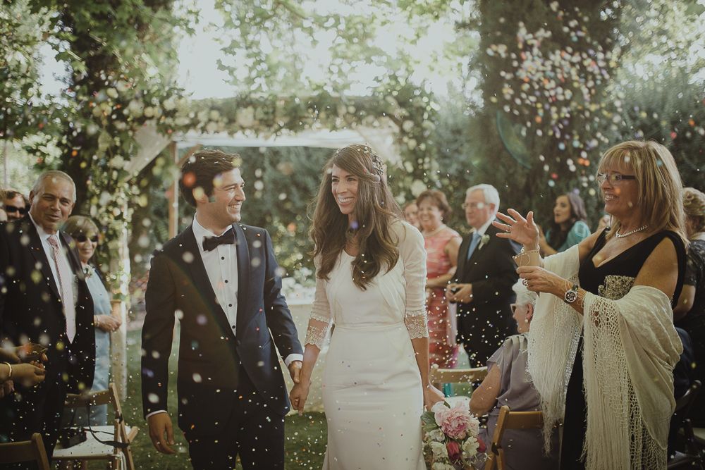 Newlyweds celebrate with confetti during outdoor garden ceremony.