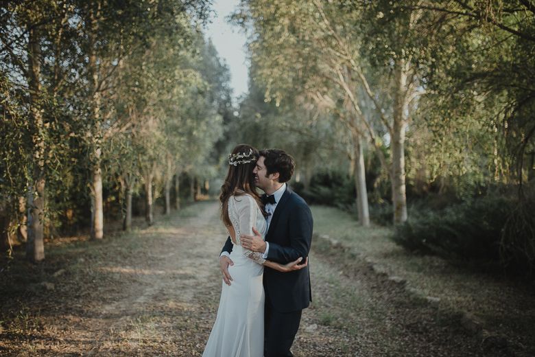 Romantic wedding couple embracing on a tree-lined path in a forest setting.