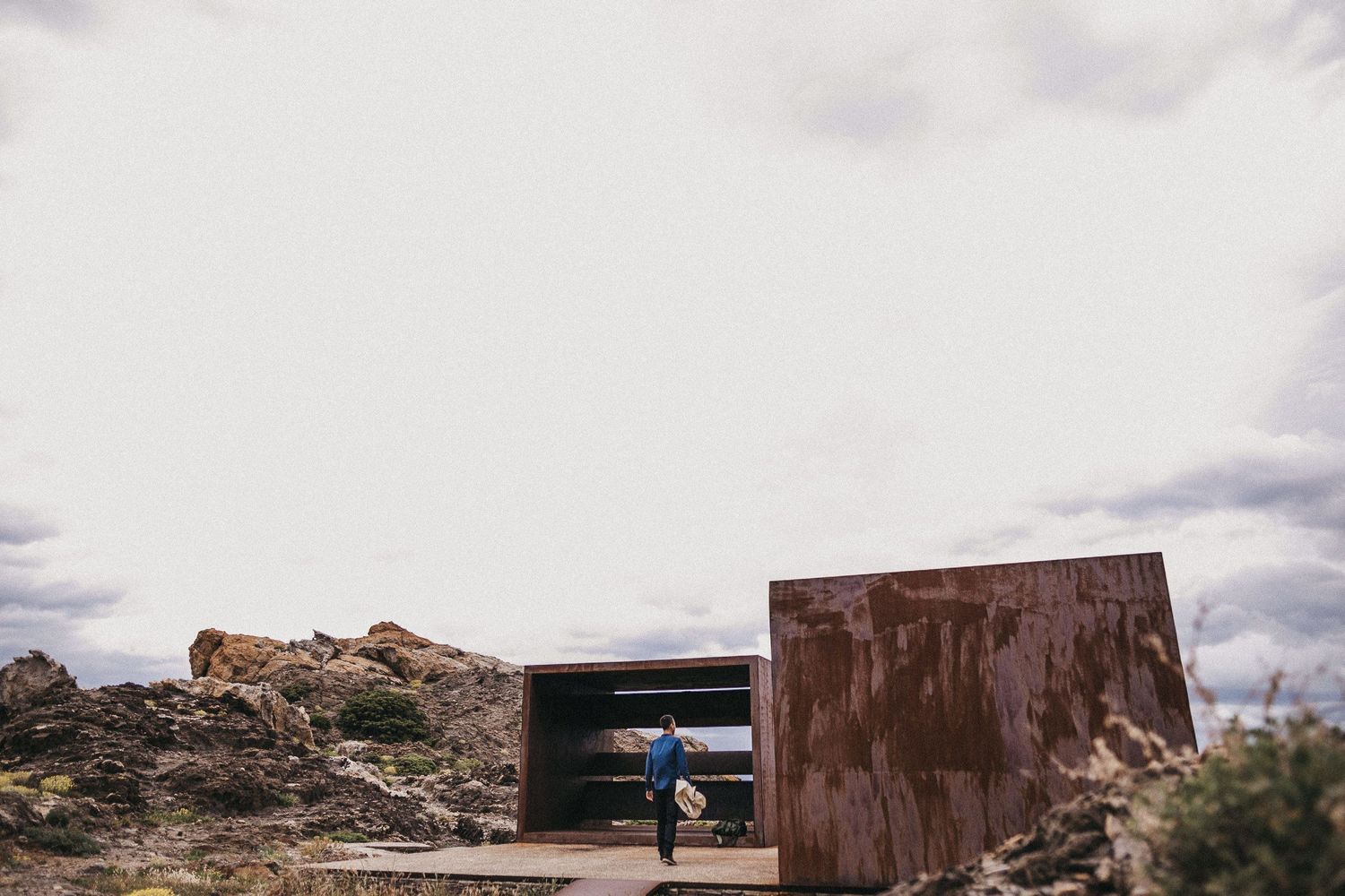 A rustic metal viewing structure frames a distant desert landscape under cloudy skies.