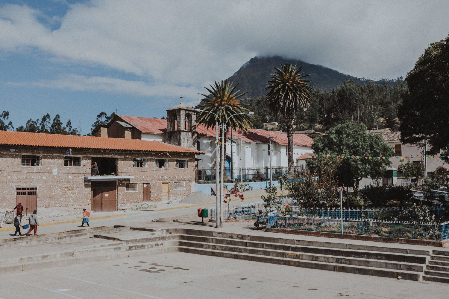Colonial architecture and palm trees frame a mountain view in a Latin American town square.
