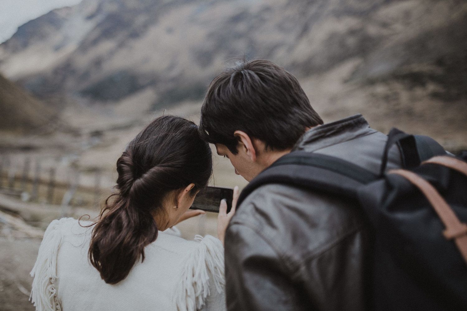Travelers in leather jackets take in the scenic mountain views on a cloudy day.
