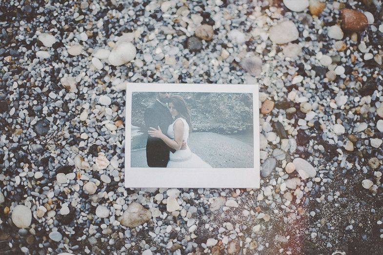 A polaroid photograph lying on a rocky surface shows a romantic beach scene.