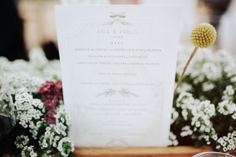 A wedding invitation displayed among white flowers and a yellow decorative ball.